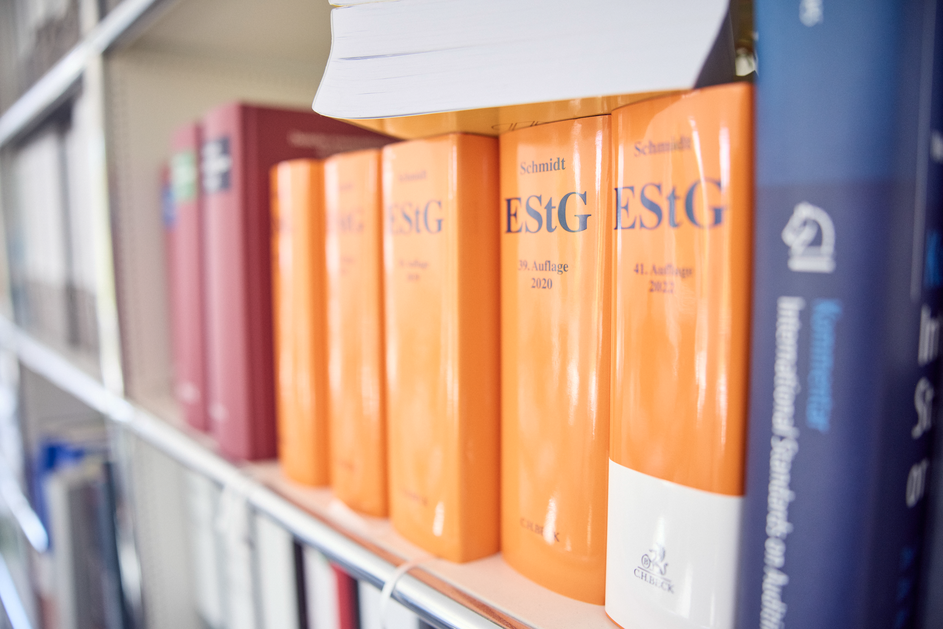 Auf einem Bücherregal sind mehrere juristische Fachbücher sichtbar, darunter orangefarbene Bände des "Schmidt ESTG" in der 41. Auflage von 2020, zwischen anderen, weniger gut sichtbaren Büchern.