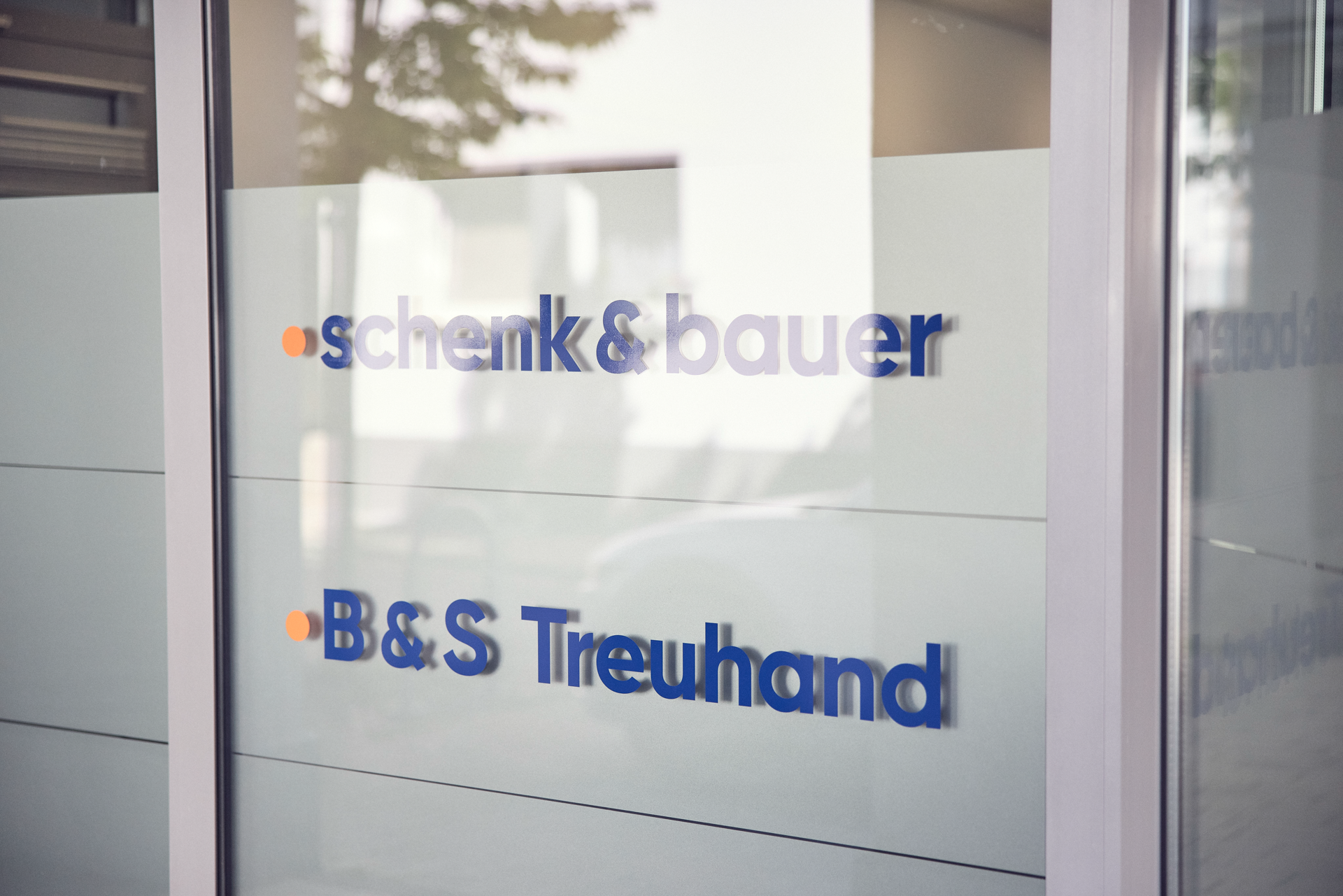 Die Glasfront zeigt die Schriftzüge "schenk&bauer" und "B&S Treuhand" in blauen Buchstaben.